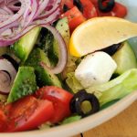 A vibrant bowl of Greek salad with fresh vegetables, feta cheese, and a lemon slice.