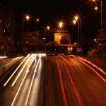Long exposure of vehicle lights creating trails on a busy Athens road at night.